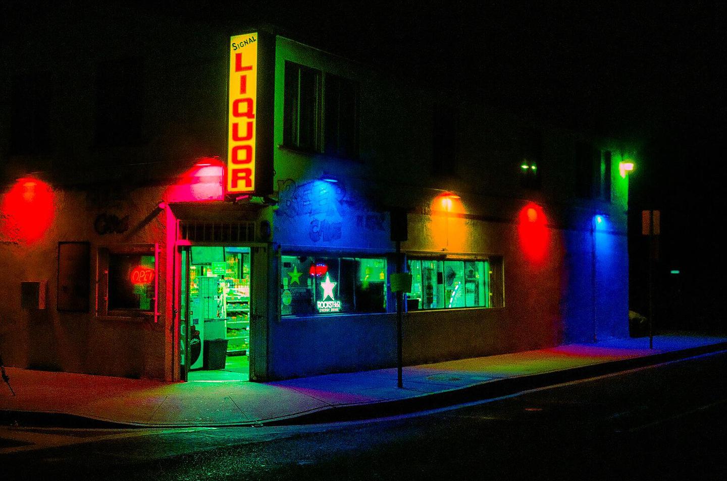 A liquor store with a bright yellow sign is illuminated by colorful neon lights at night.
