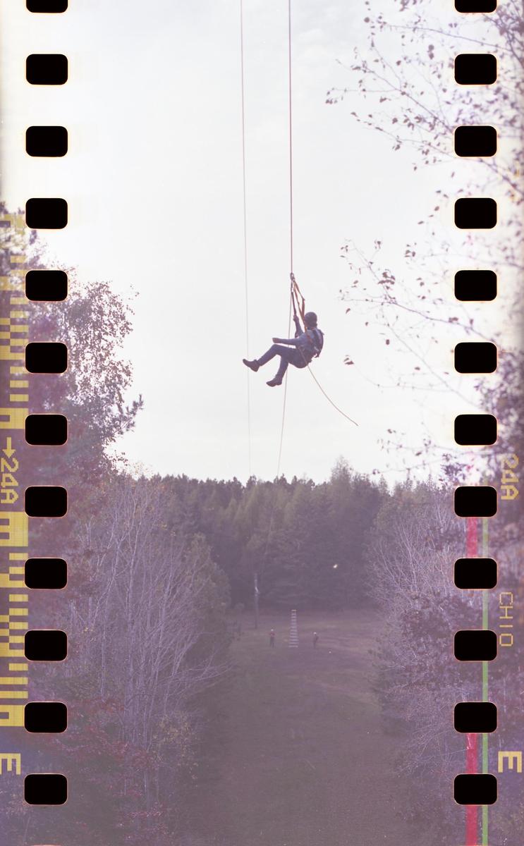 A person hangs from a zip line above a forest.
