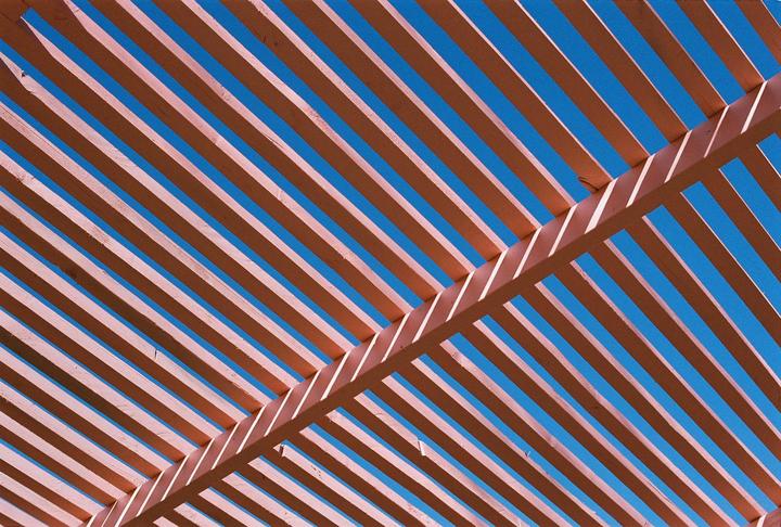 A wooden pergola casts shadows against a bright blue sky.
