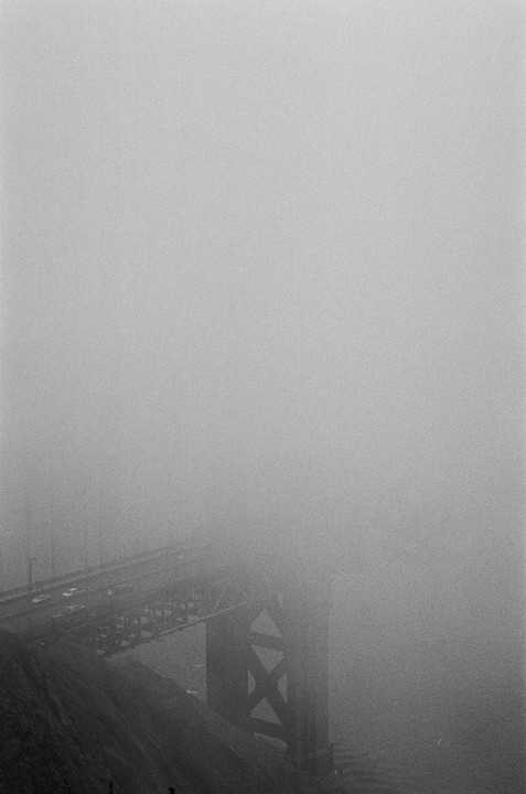 A bridge is barely visible through thick fog.