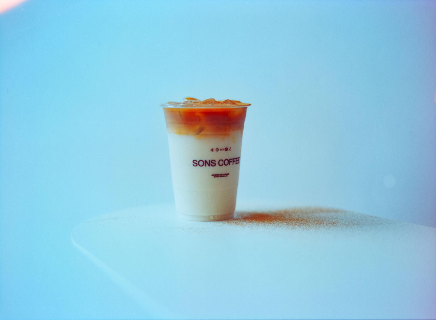 A plastic cup of iced coffee with milk is on a white surface with a blue background.
