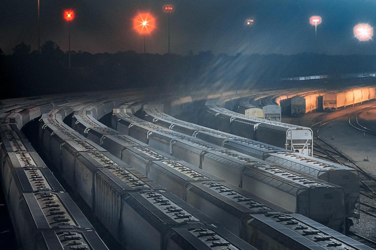 Numerous train cars are parked on curved tracks at night, illuminated by distant red and orange lights.