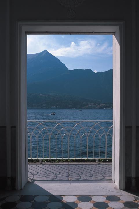 A view of a lake and mountains is framed by a doorway and a white railing.