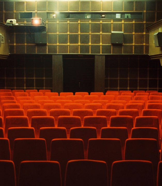 Rows of empty red seats face a dark wall with a projector shining a light.