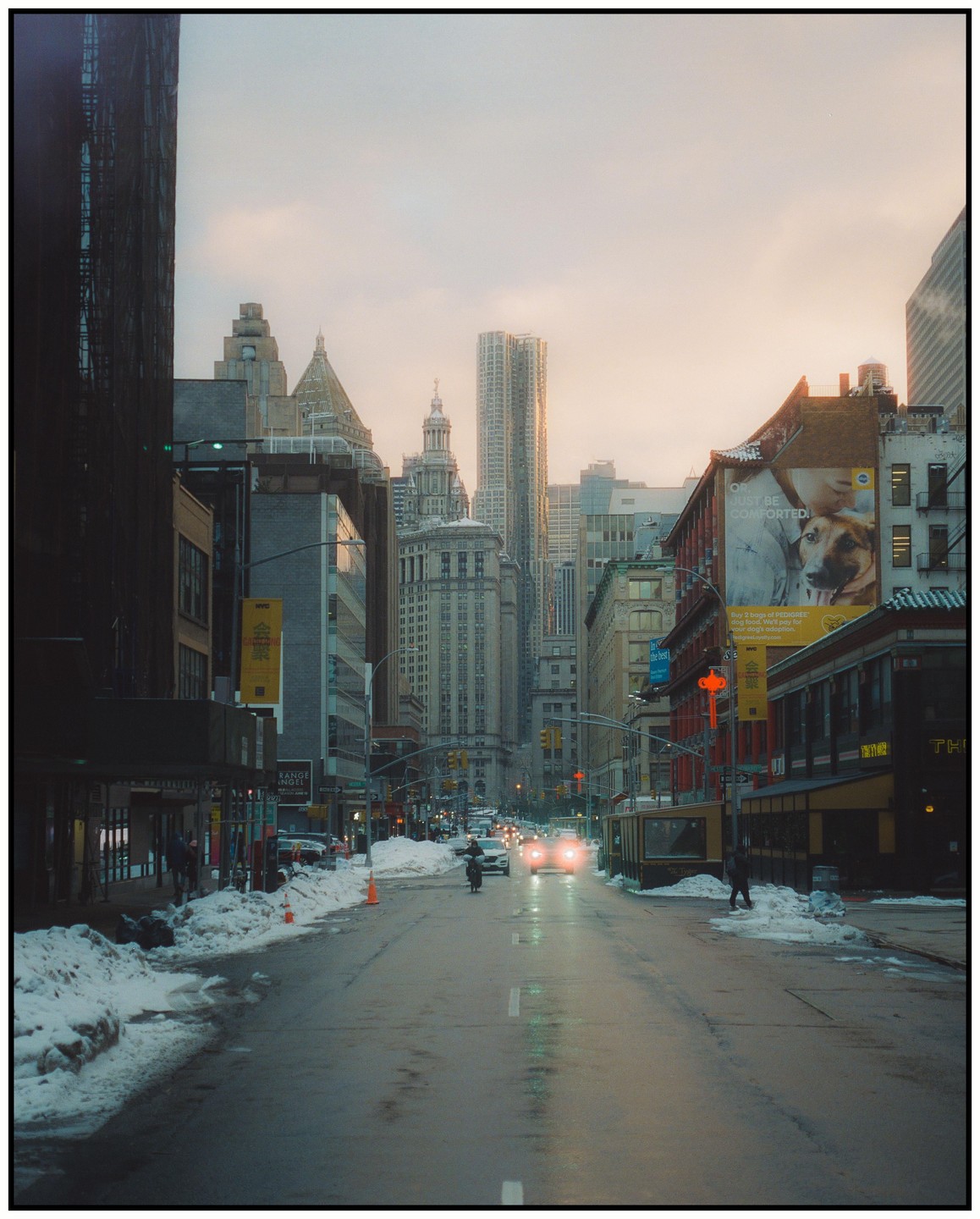 A street in a city is covered in snow and slush with cars driving down it and tall buildings on either side.
