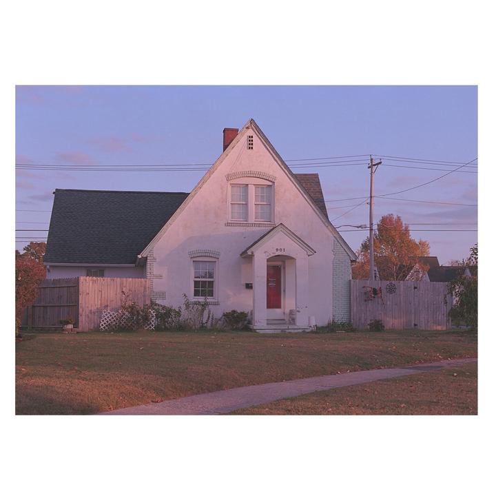 A white house with a red door and a green roof stands under a purple sky.