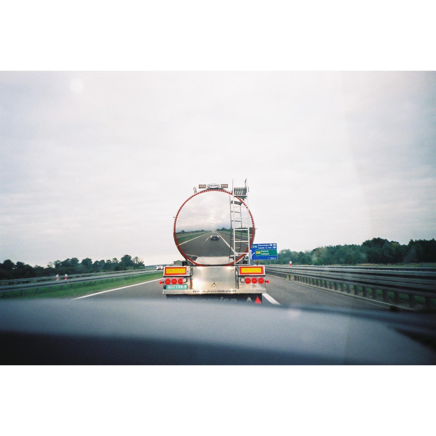 A tanker truck is driving on a highway under a cloudy sky.