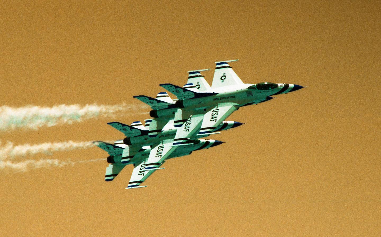 Four fighter jets fly in formation against an orange sky, leaving white contrails.
