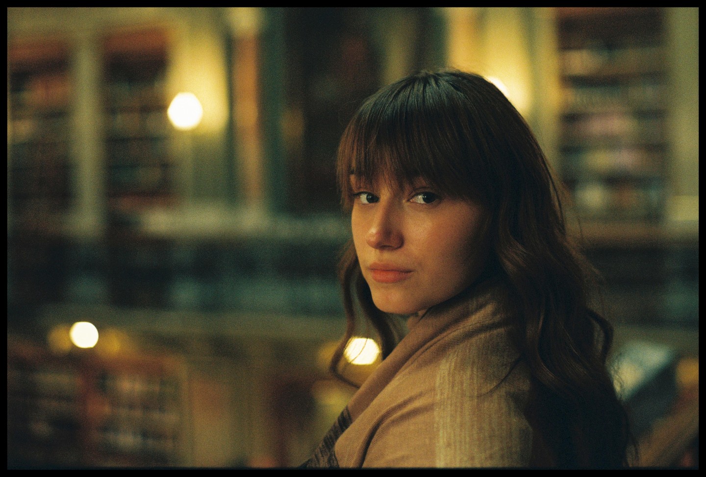 A woman with long hair and bangs looks over her shoulder at the viewer.