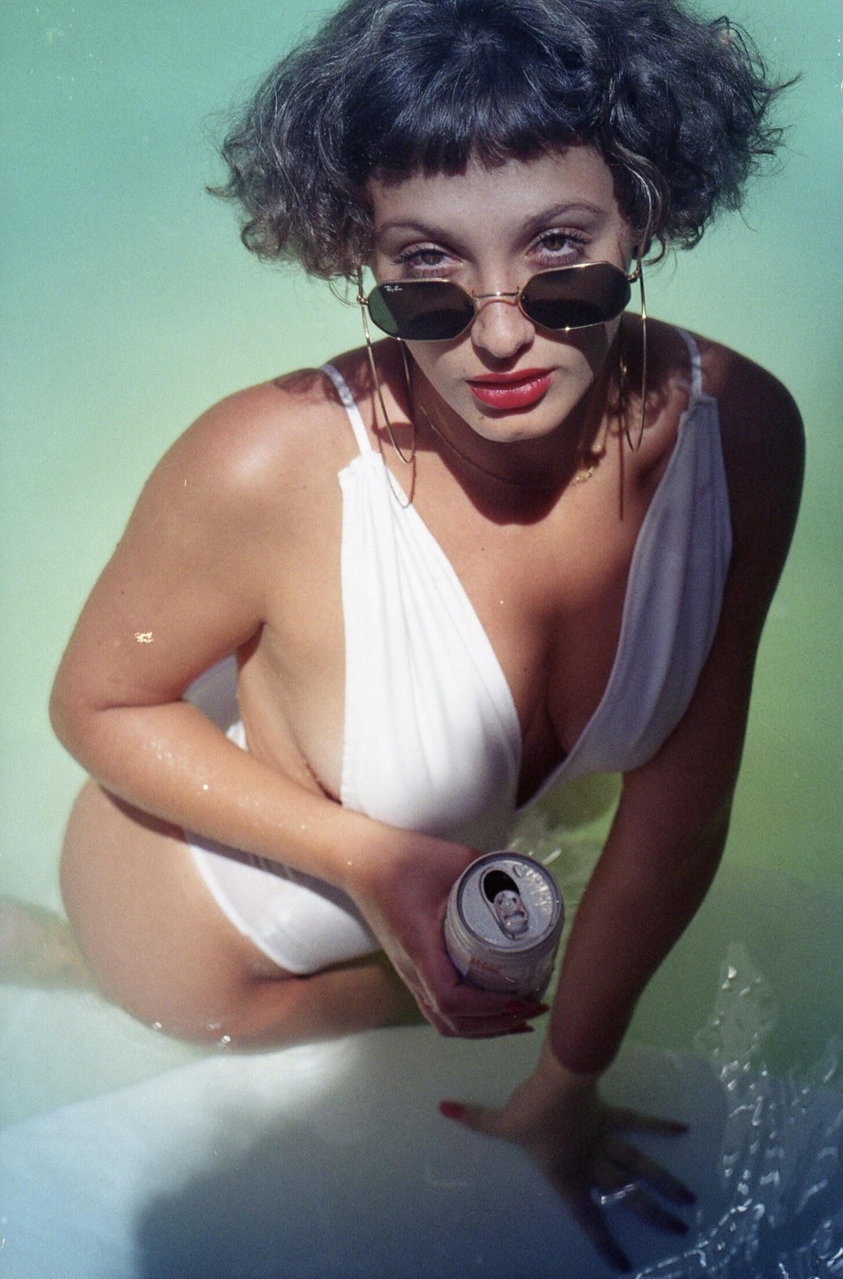 A woman in a white swimsuit and sunglasses is in water, holding a can.