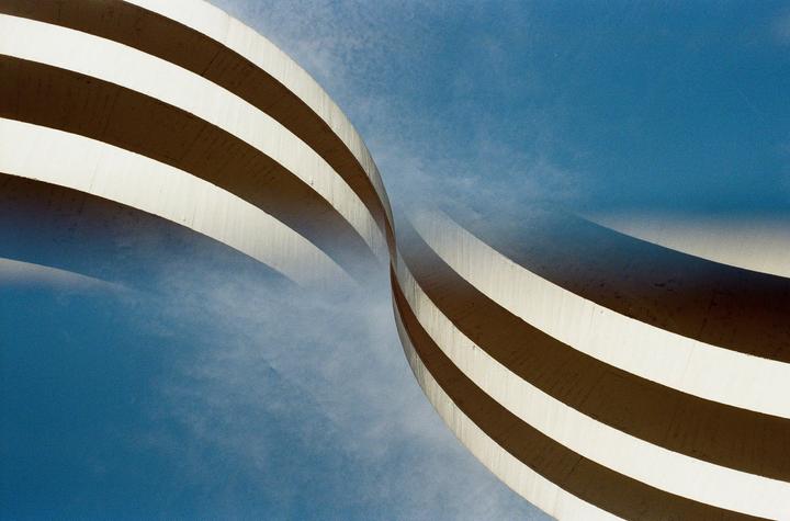 Two curved concrete structures with horizontal stripes are visible against a blue sky.