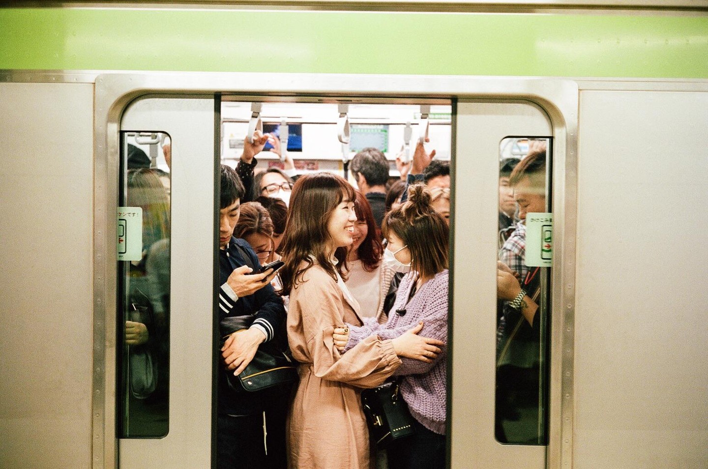 Two women embrace and smile in a crowded train car.