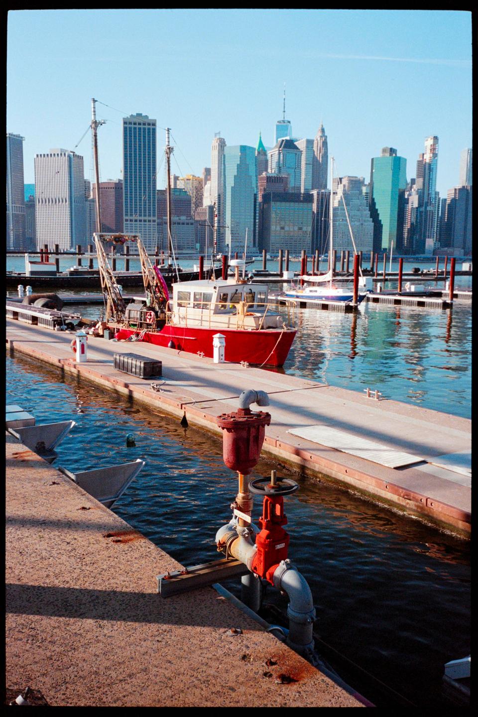 A red boat is docked at a pier with a city skyline in the background.