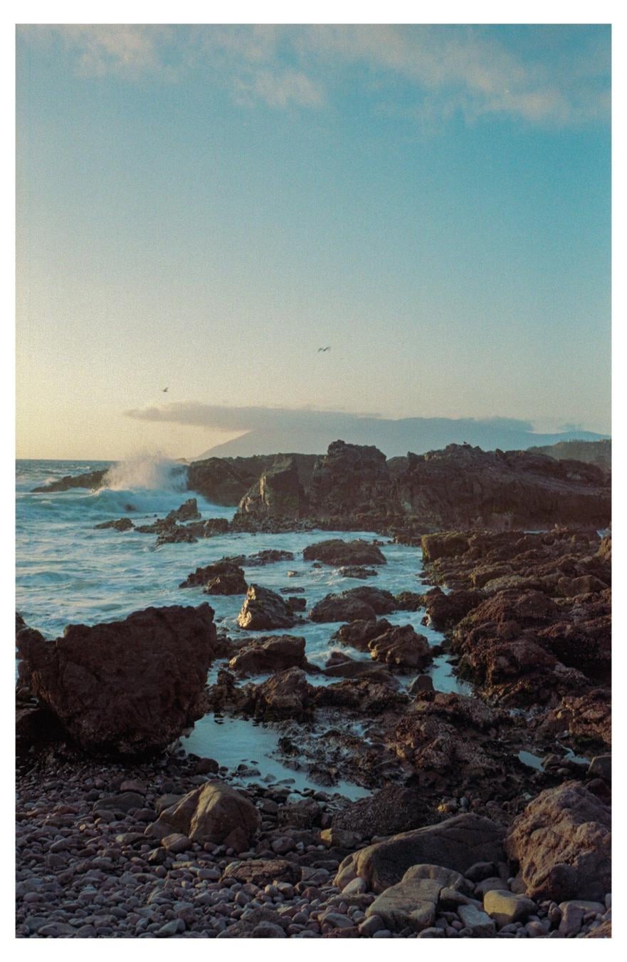 Waves crash against a rocky shore under a clear sky with a few clouds.