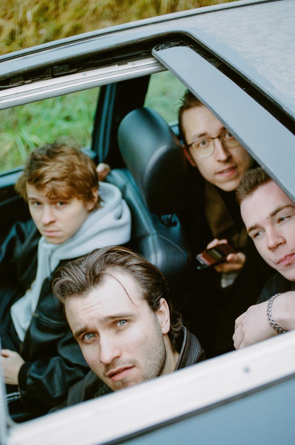 Four men are looking out of a car with an open sunroof.