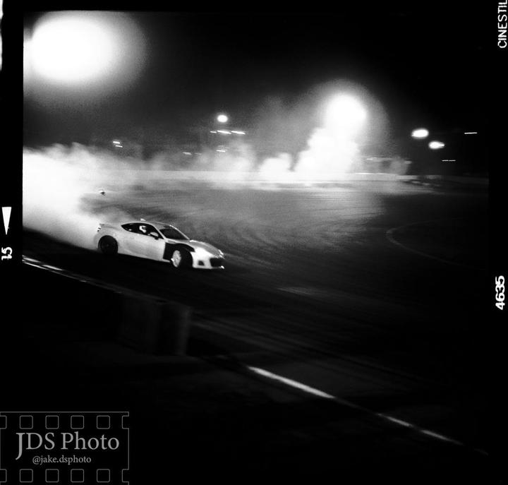 A white car drifts on a track at night, creating a large cloud of smoke.