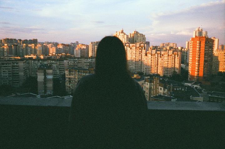 A person stands on a rooftop overlooking a city at golden hour.