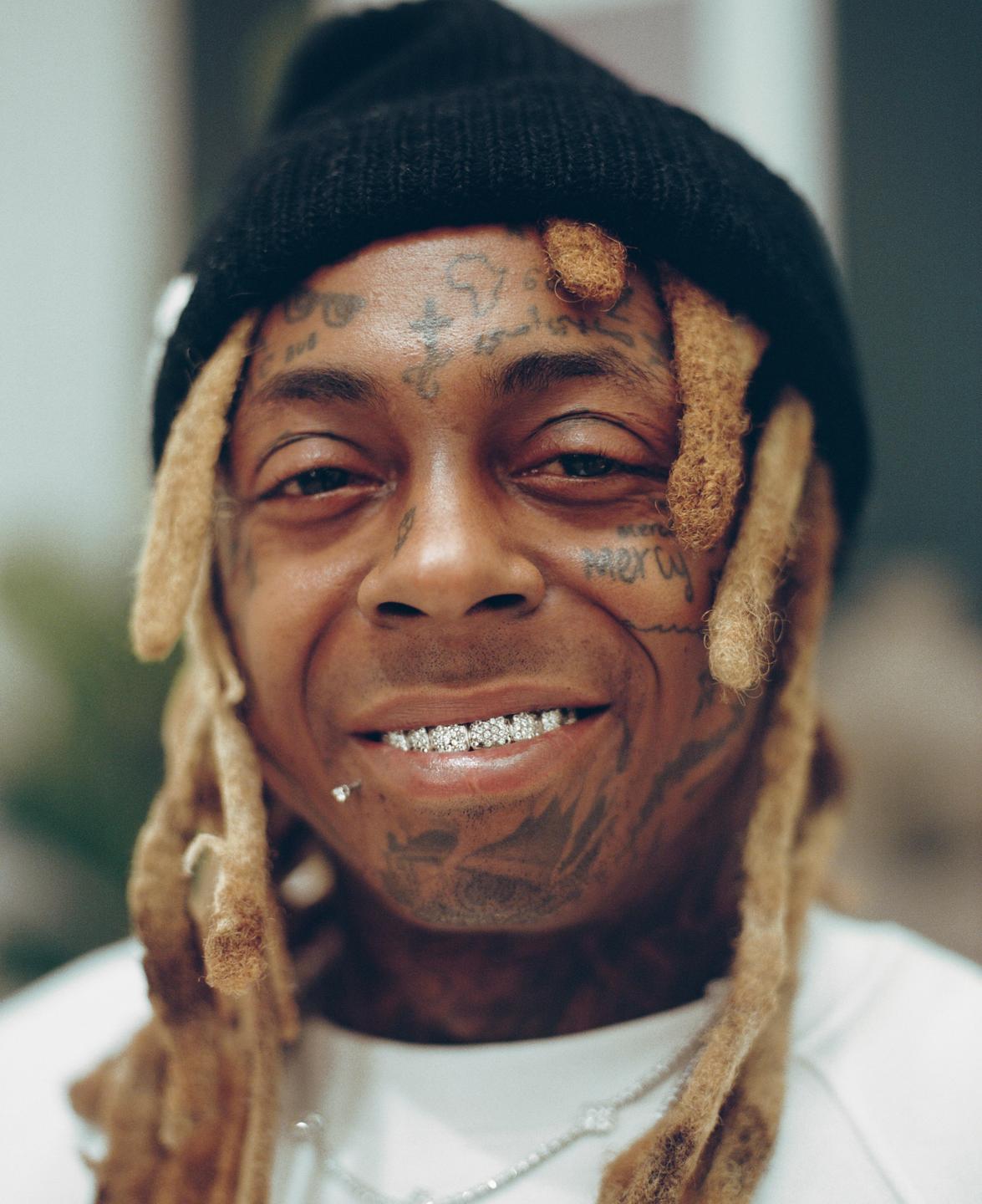 A man with dreadlocks and facial tattoos smiles at the camera, wearing a black beanie and a diamond grill.