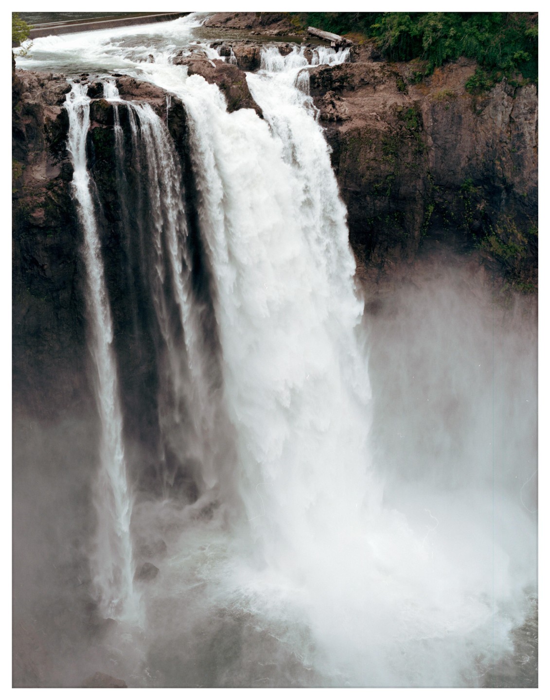 A powerful waterfall cascades over a rocky cliff, creating a misty spray at its base.