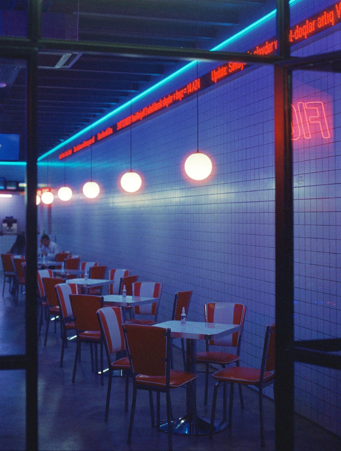 A diner with red and white chairs and tables is illuminated by neon lights and hanging globe lamps.