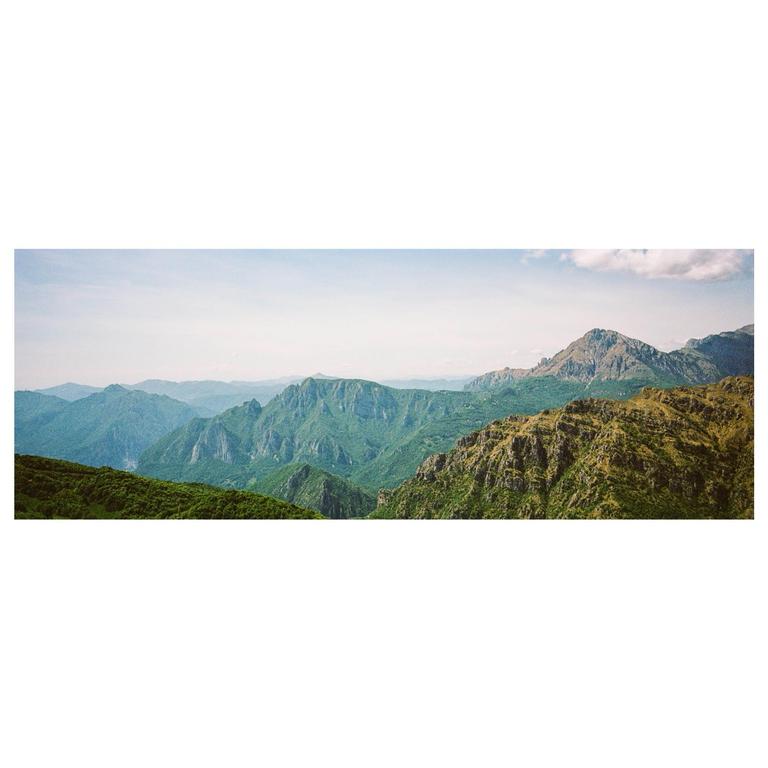 A panoramic landscape shows a valley with green mountains under a bright sky.