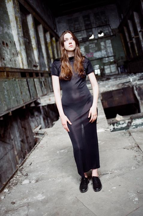 A woman in a black dress stands in a derelict industrial building.