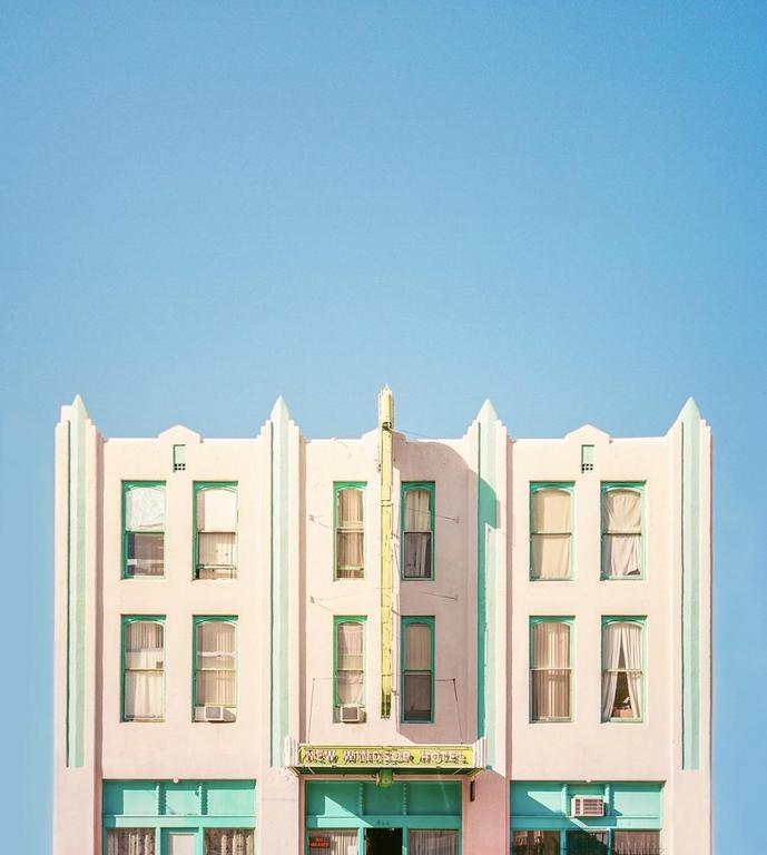 A pastel pink and mint green art deco building with a yellow sign is visible against a clear blue sky.