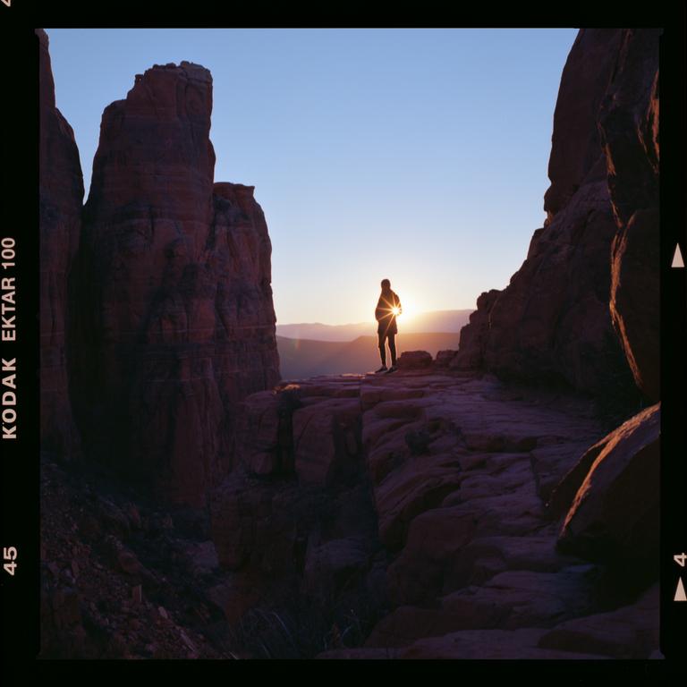 A person stands on a rock formation at sunset, with mountains in the distance.