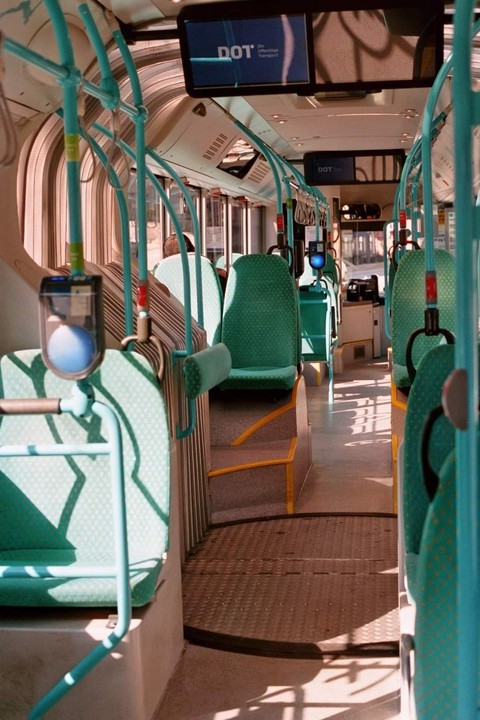 The interior of a bus is visible, with rows of empty seats and sunlight casting shadows on the floor.