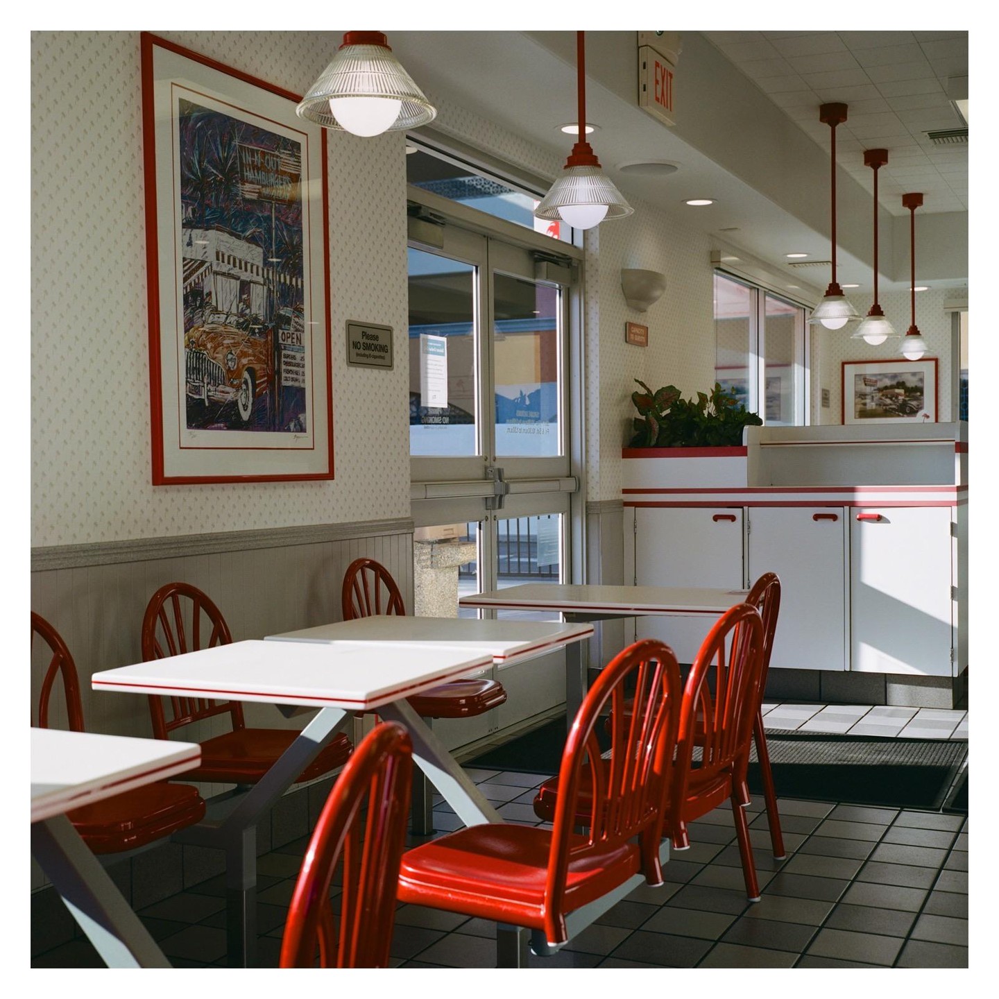 A diner interior features red chairs and white tables, with sunlight streaming through a glass door.