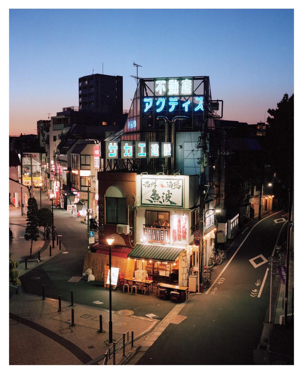 A street corner in Tokyo is illuminated by neon signs and streetlights at dusk.