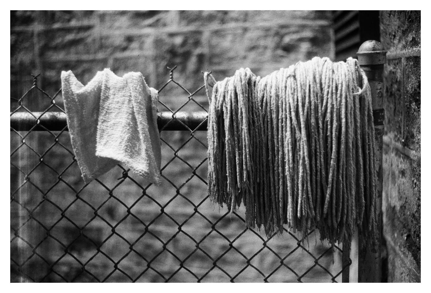 A towel and a mop hang on a chain link fence.