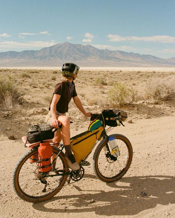 A person on a bicycle looks out at a vast desert landscape with mountains in the distance.