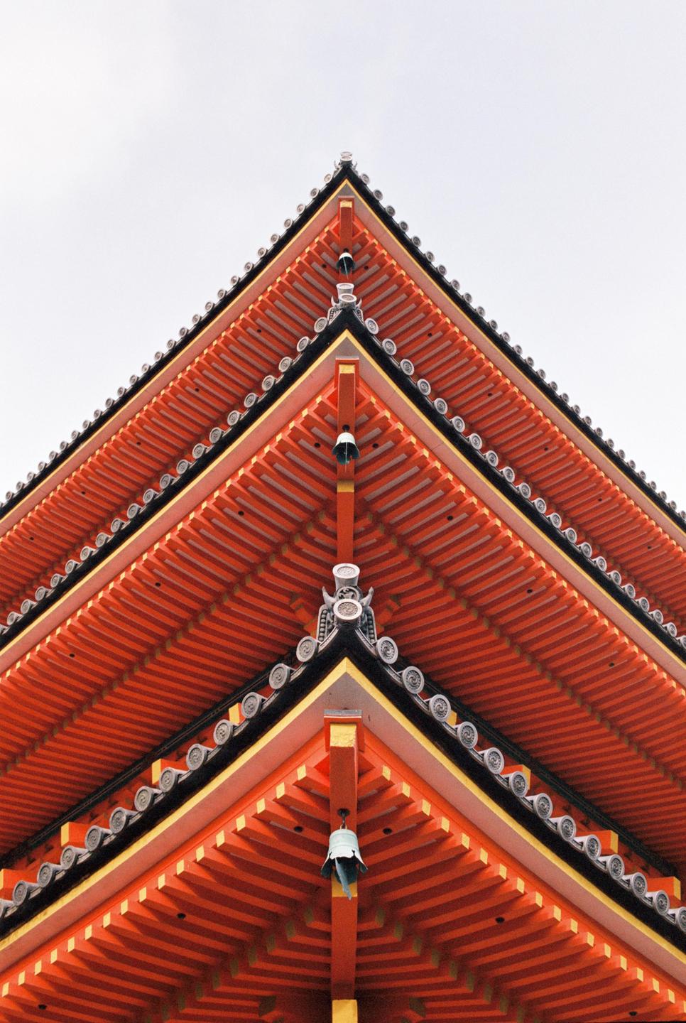 A low-angle view shows the corner of a multi-tiered pagoda roof with orange eaves and a small bell hanging from one of the corners.