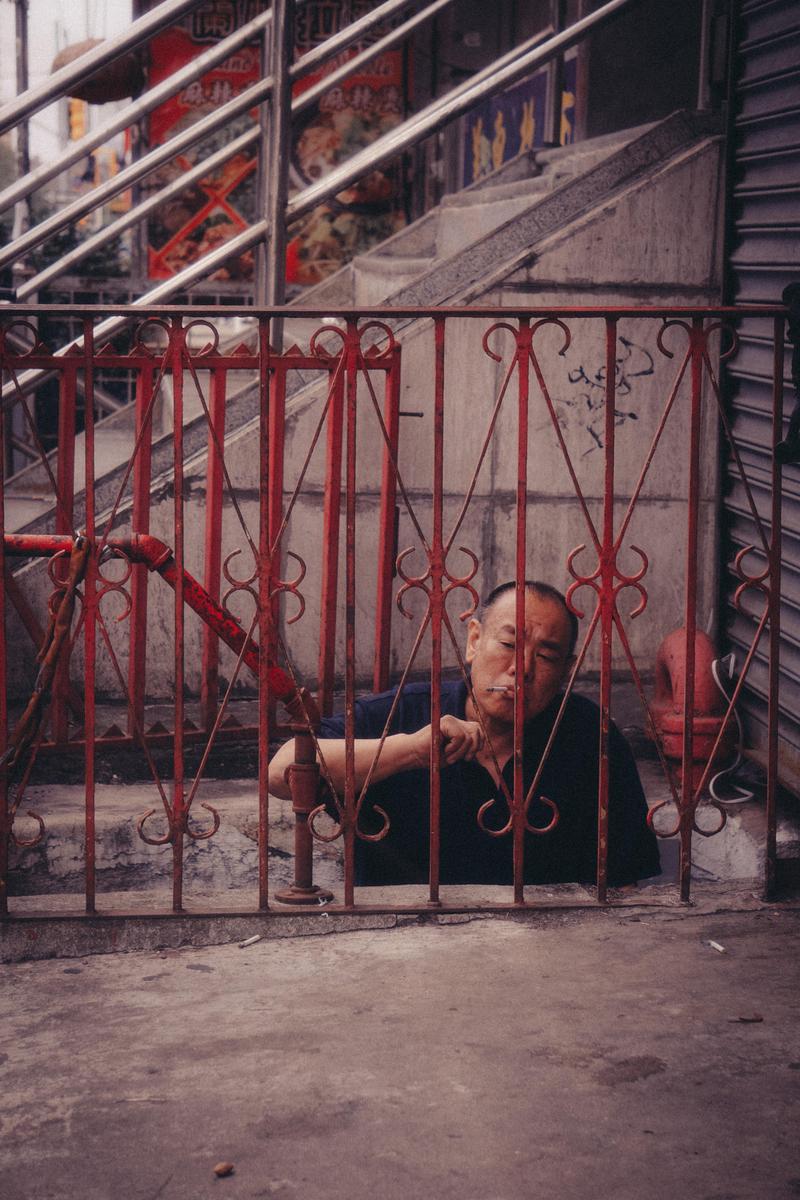 A man is visible behind a red metal fence on a street in Chinatown, New York City.