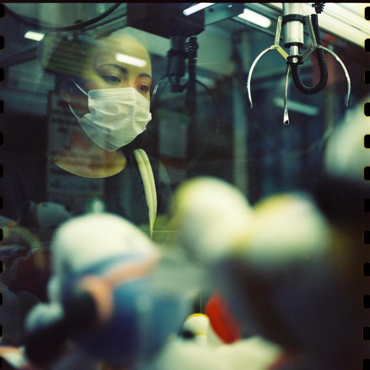 A woman in a face mask looks into a claw machine filled with plush toys.