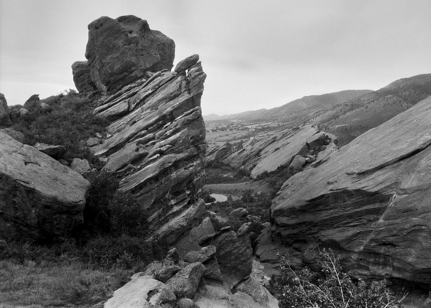 A black and white landscape shows large rock formations and distant hills under a cloudy sky.