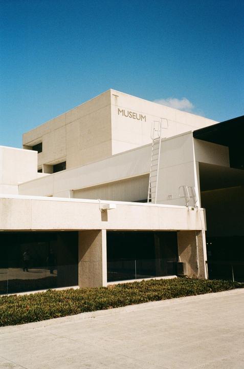 A white museum building with the word "MUSEUM" on its facade stands under a clear blue sky.