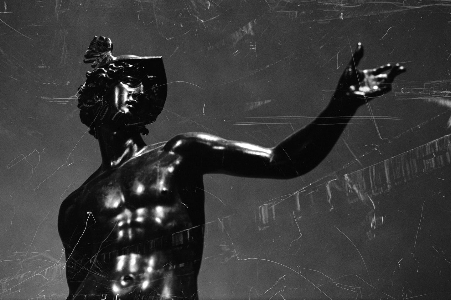 A statue of a man wearing a helmet with a winged ornament on top is shown with his arm outstretched.