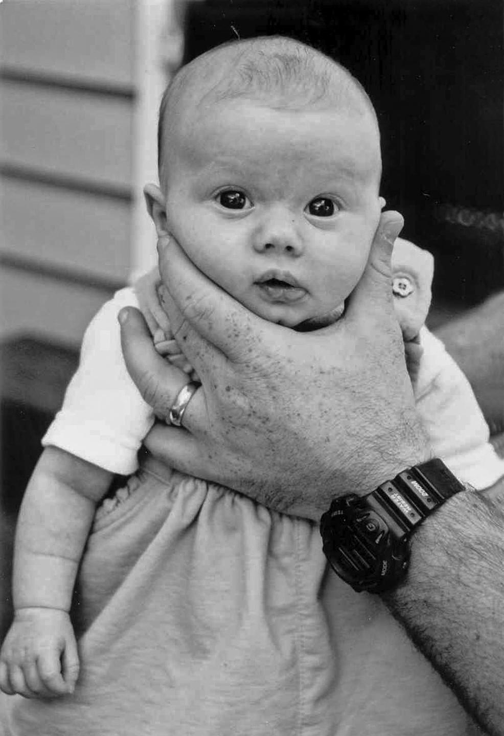 A baby is held by a man's hand, which has a ring and a watch.