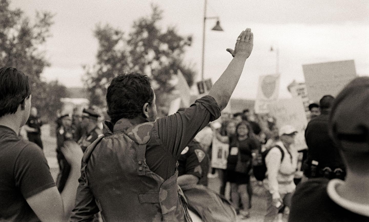 A man with his arm raised stands in a crowd of people, some holding signs.