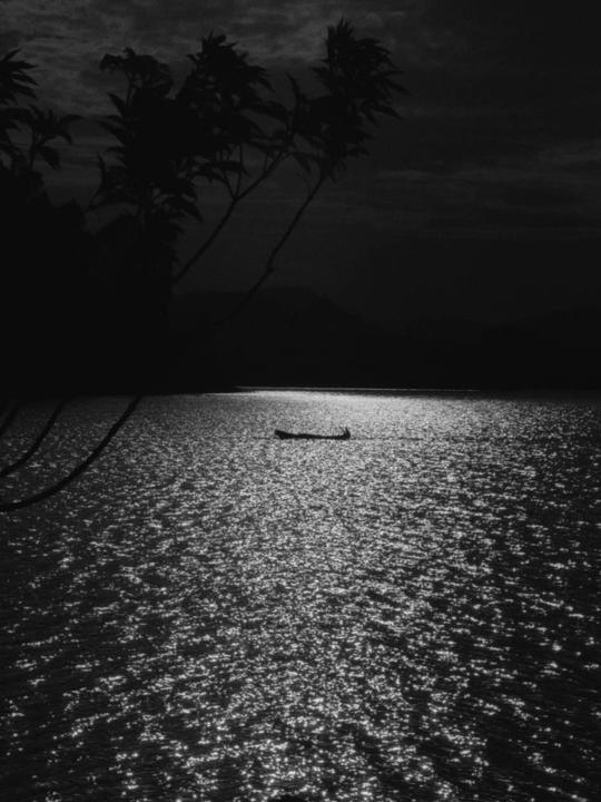 A small boat floats on a body of water under a dark sky, with light reflecting off the water.