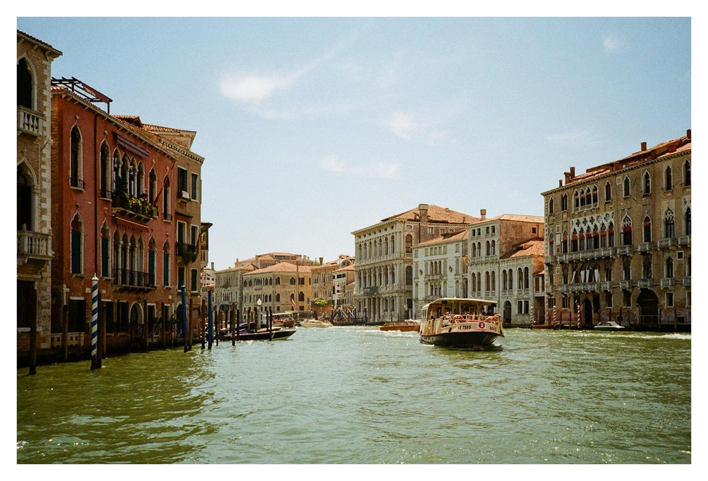 A boat travels down a canal lined with historic buildings under a clear sky.