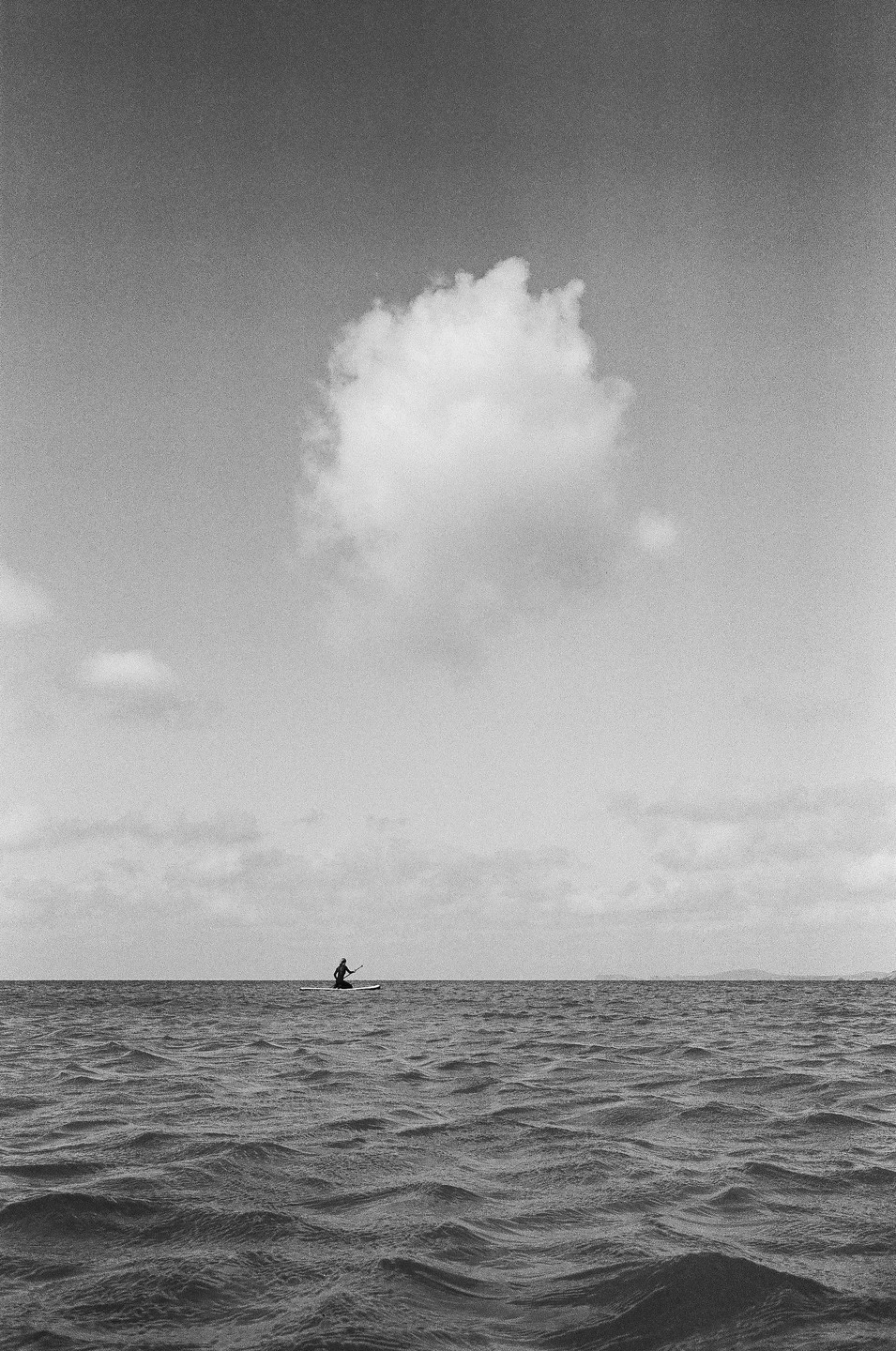 A person on a paddleboard is on the open water under a large cloud.