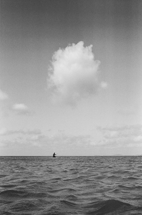 A person on a paddleboard is on the open water under a large cloud.