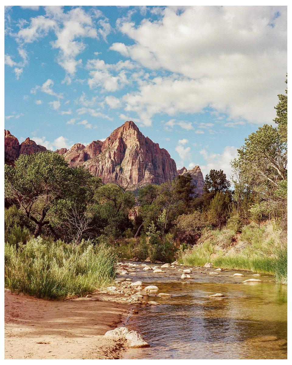 A river flows through a valley with mountains and trees under a cloudy sky.