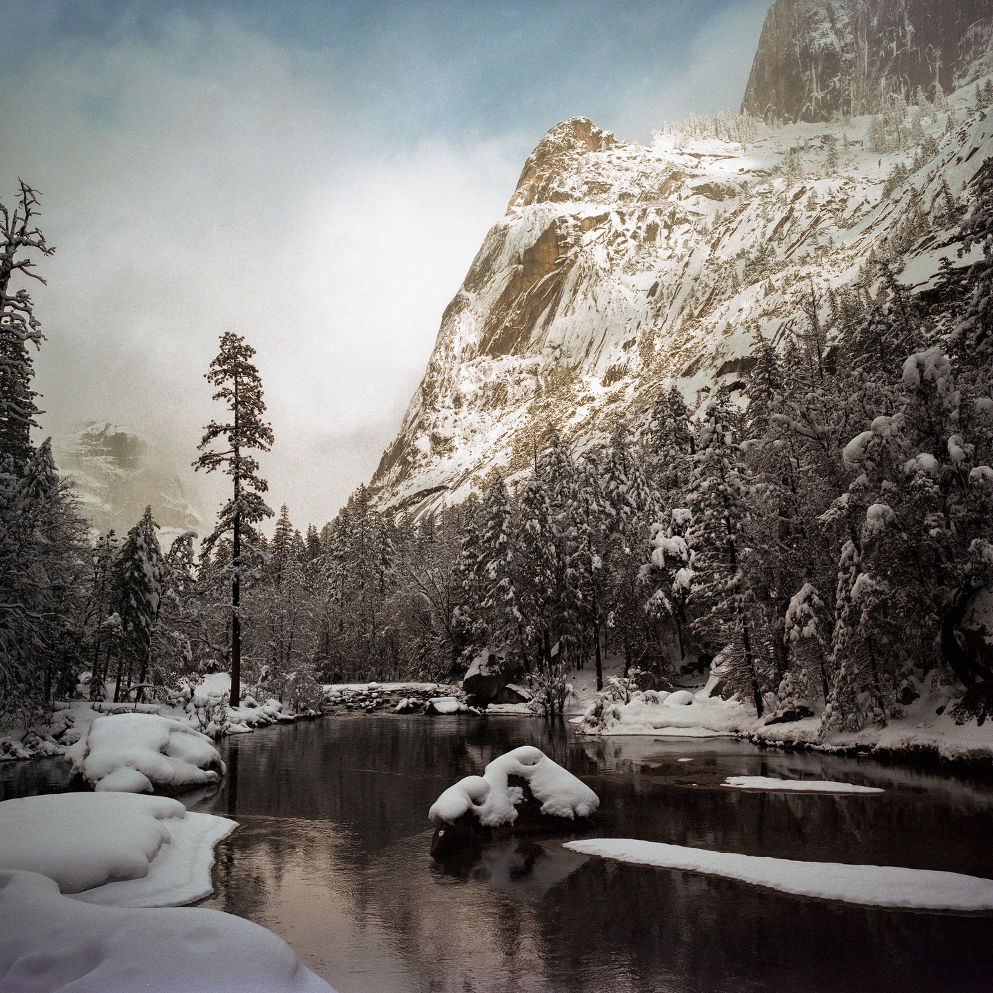 A snow-covered mountain rises above a river surrounded by snow-covered trees.