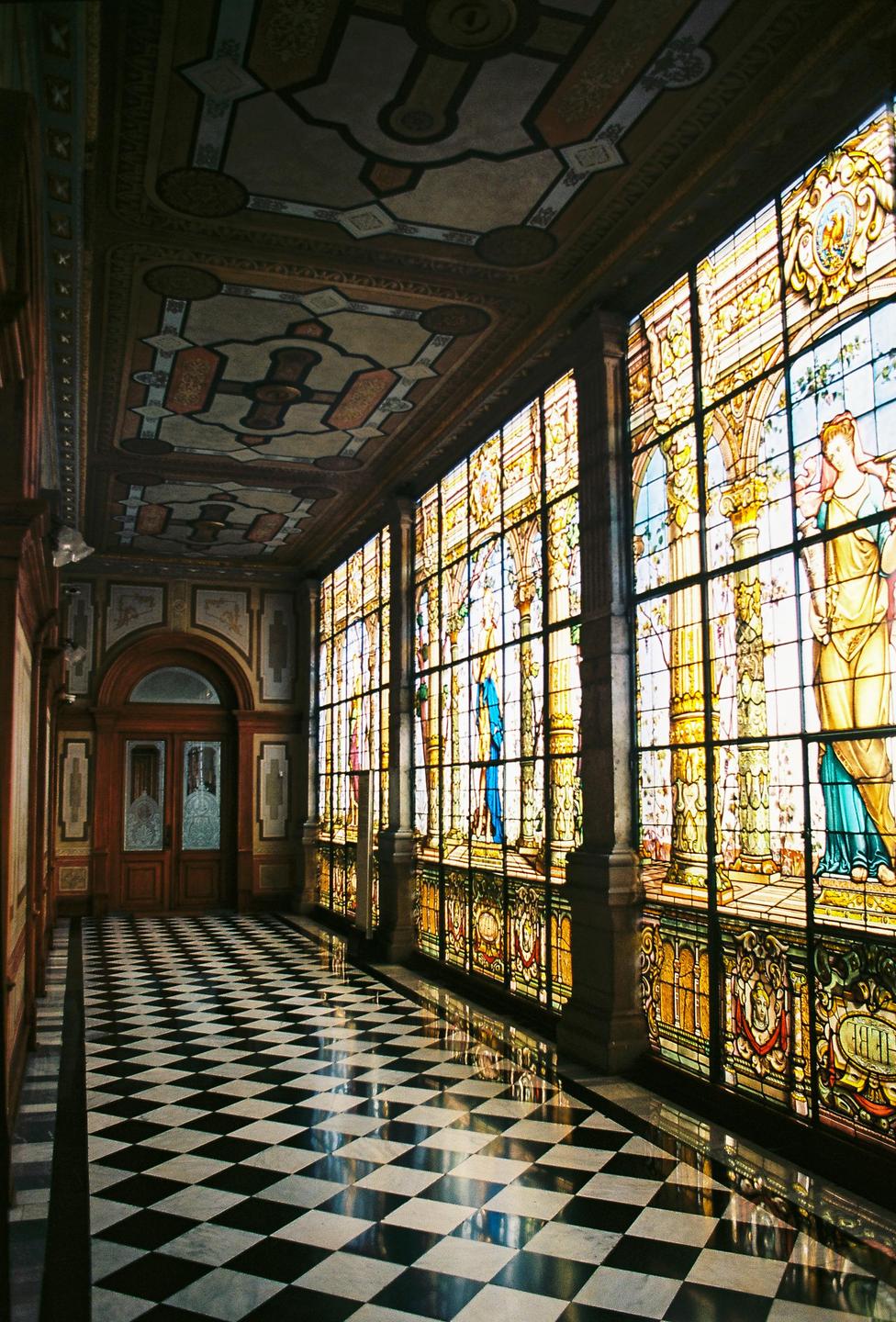 A long hallway with a checkered floor and a wall of stained glass windows is visible.