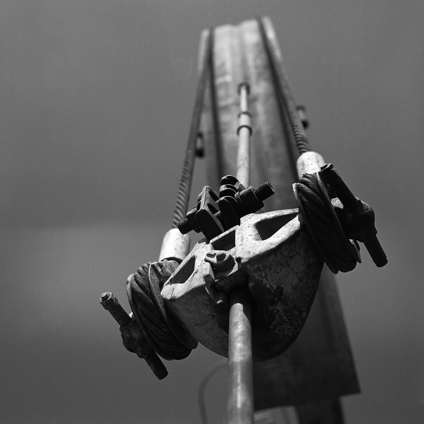 A low-angle, black and white shot shows a metal horsehead with cables and bolts against a plain sky.