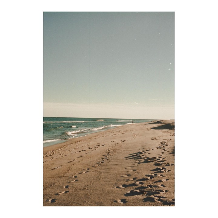 A person walks along a sandy beach with footprints in the sand and waves crashing on the shore.